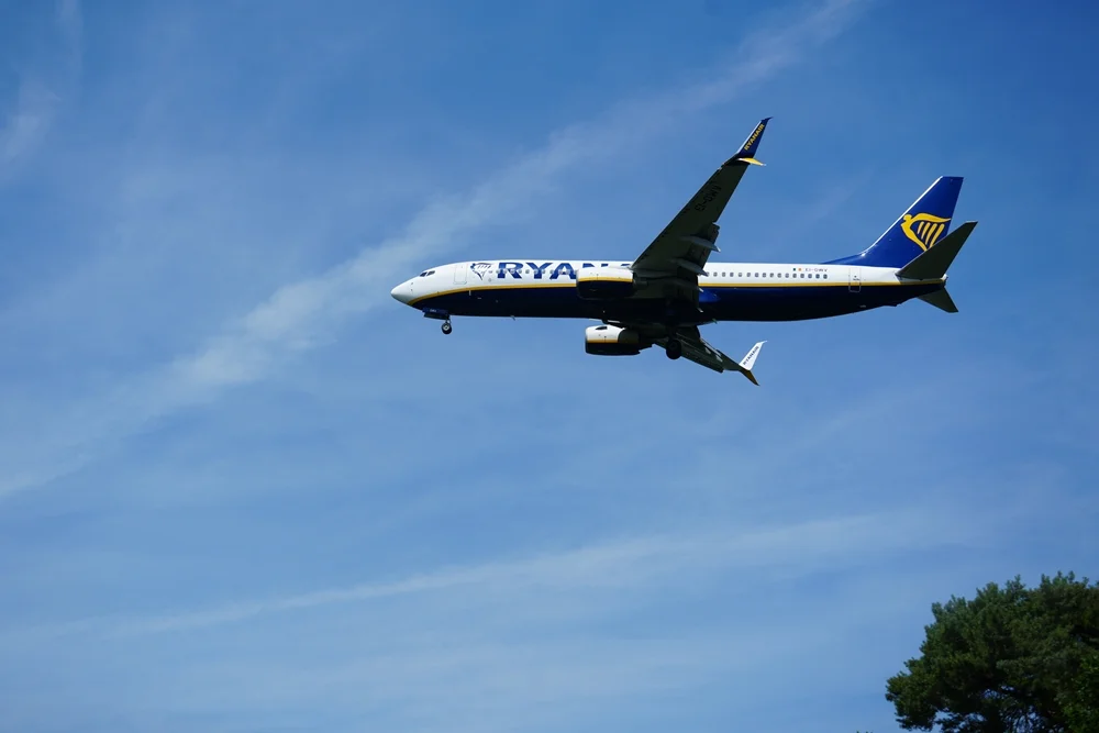 Ryanair-Flugzeug mit ausgefahrenem Fahrwerk im Landeanflug unter blauem Himmel.