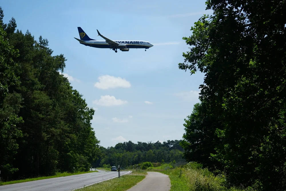 Ryanair Boeing 737 im Endanflug auf den Airport Weeze über der Kevelaerer Straße, eingerahmt von hohen Bäumen und sommerlicher Landschaft.