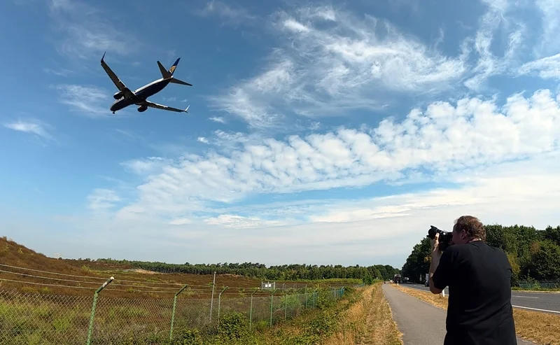 Making-of-Foto einer Flugzeugaufnahme am Flughafen Weeze. Ein Fotograf richtet seine Kamera auf ein tief über ihm fliegendes Passagierflugzeug.