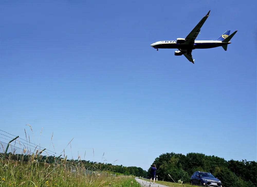 Making-of-Foto am Flughafen Weeze. Ein Fotograf richtet seine Kamera auf ein tief anfliegendes Passagierflugzeug.