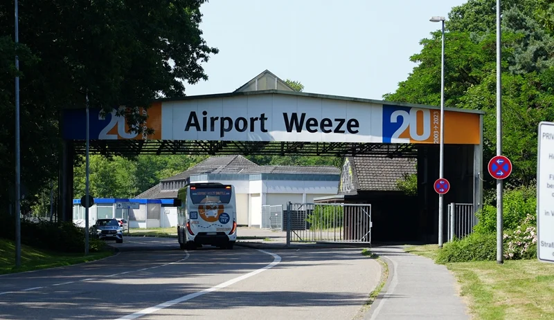 Blick auf die Zufahrt zum Flughafen Weeze. Ein Linienbus fährt unter dem markanten Airport-Weeze-Tor auf das Flughafengelände.