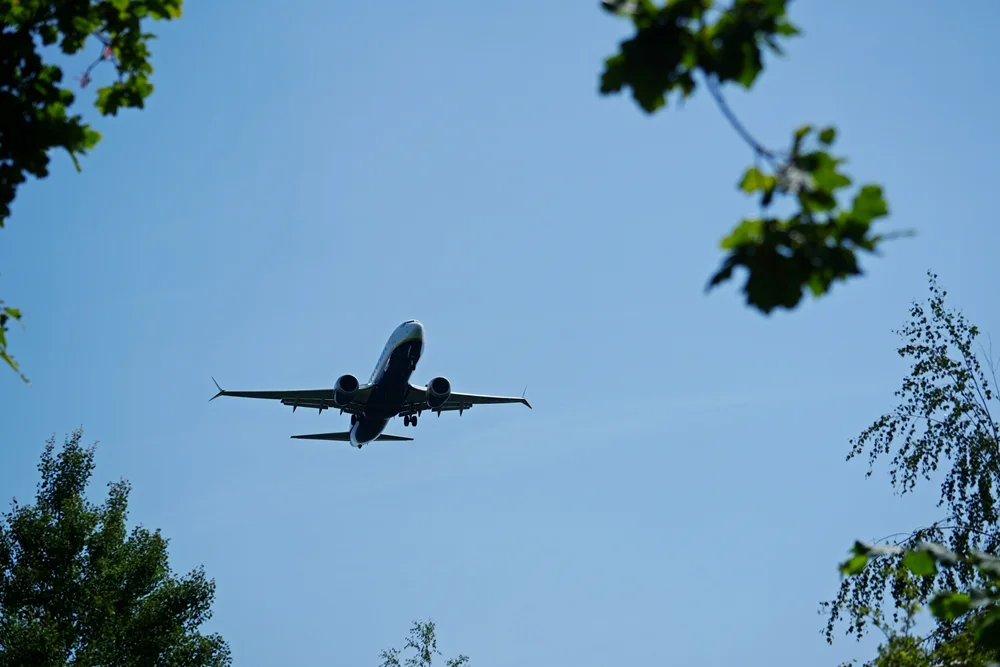 Blick durch die Bäume auf ein Passagierflugzeug im Landeanflug auf den Flughafen Weeze. Das Fahrwerk ist bereits ausgefahren.