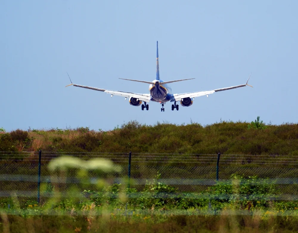 Ryanair-Flugzeug kurz vor der Landung am Flughafen Weeze. Die Maschine fliegt mit ausgefahrenem Fahrwerk über die Begrünung am Rand der Start- und Landebahn.