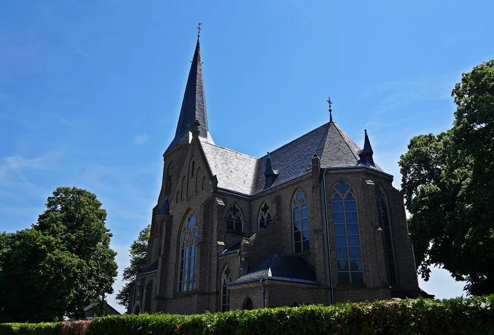 Seitenansicht der katholischen Kirche in Wemb. Der hohe Kirchturm und die großen Kirchenfenster prägen das historische Backsteingebäude.