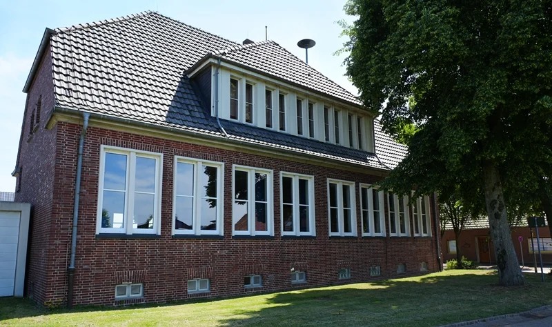 Blick auf die Rückseite der Christophorus-Schule in Wemb. Das historische Backsteingebäude wird von einer Rasenfläche und großen Bäumen umgeben.