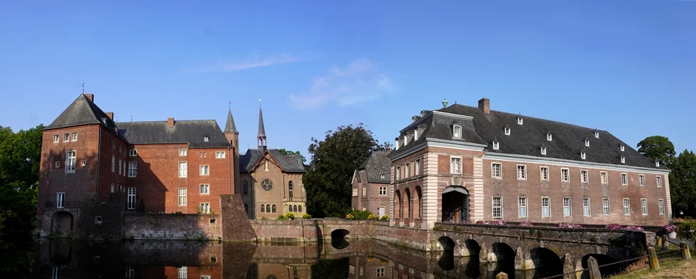 Panoramablick auf Schloss Wissen in Weeze mit den historischen Backsteingebäuden, der Brücke und den Spiegelungen im Wassergraben.