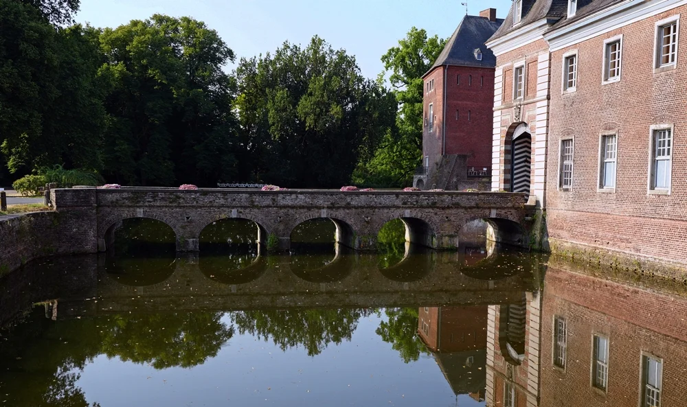 Die Schlossbrücke von Schloss Wissen in Weeze mit ihren Rundbögen und der Spiegelung im ruhigen Wassergraben.