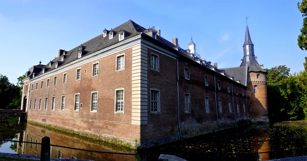 Das lange Backsteingebäude von Schloss Wissen in Weeze mit dem Eckturm und dem umlaufenden Wassergraben.