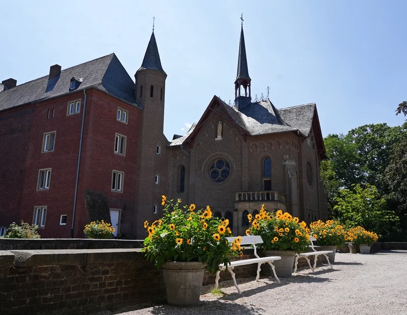 Kapelle von Schloss Wissen in Weeze mit Sonnenblumen und weißen Bänken