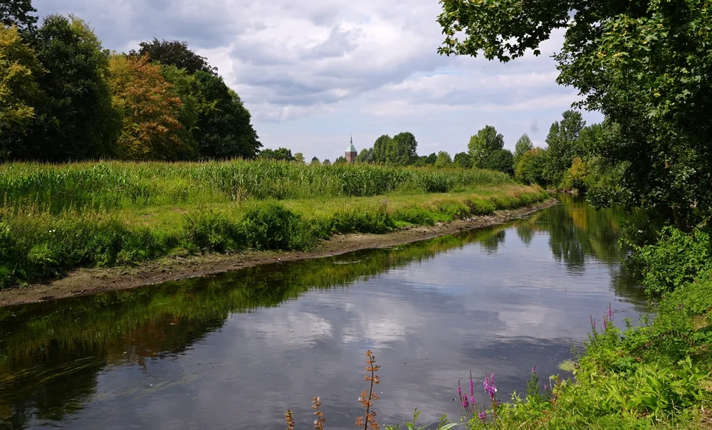 Die Niers bei Weeze mit Wiesen und dem Kirchturm von St. Cyriakus im Hintergrund