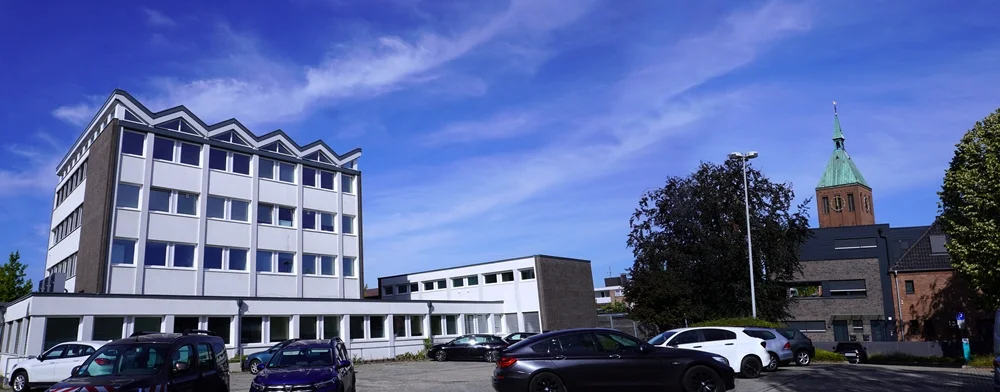 Rückansicht des Weezer Rathauses mit Parkplatz und dem Kirchturm von St. Cyriakus im Hintergrund