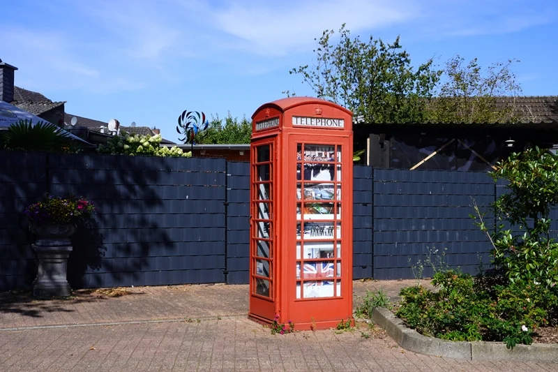 Alte rote englische Telefonzelle in Weeze vor einer dunklen Gartenmauer