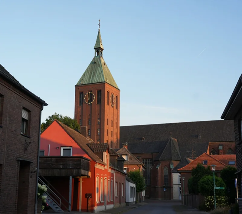 Blick durch eine Weezer Straße auf den Kirchturm der St.-Cyriakus-Kirche im warmen Morgenlicht
