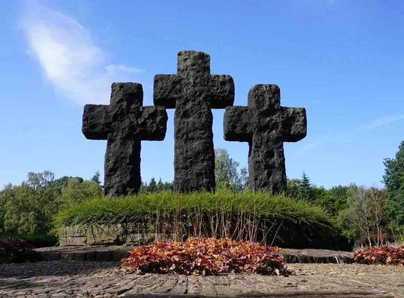 Drei monumentale Steinkreuze auf der gepflegten Kriegsgräberstätte in Weeze vor blauem Himmel