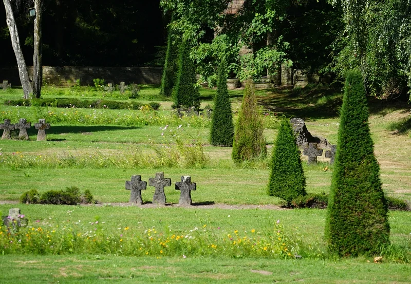 Steinkreuze zwischen Blumenwiesen und gepflegten Bäumen auf der Kriegsgräberstätte in Weeze