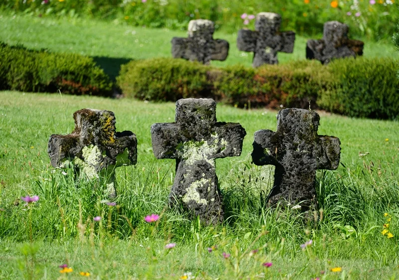 Nahaufnahme verwitterter Steinkreuze zwischen Gras und Blumen auf der Kriegsgräberstätte in Weeze