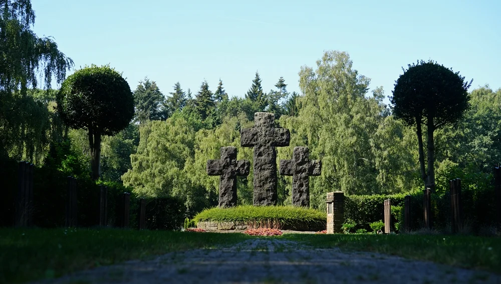Blick über den Weg auf die drei großen Steinkreuze der Kriegsgräberstätte in Weeze