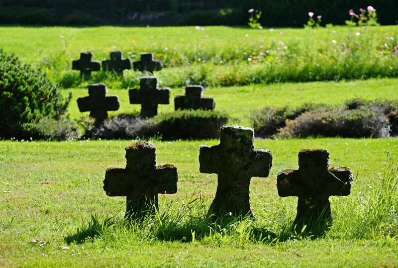 Mehrere verwitterte Steinkreuze zwischen grünen Wiesen und Blumen auf der Kriegsgräberstätte in Weeze