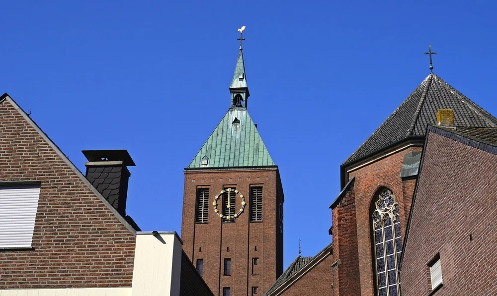 Kirchturm der St.-Cyriakus-Kirche in Weeze mit Wetterhahn zwischen den umliegenden Gebäuden