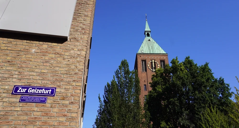 Straßenschild Zur Geizefurt mit dem Kirchturm der St.-Cyriakus-Kirche in Weeze im Hintergrund