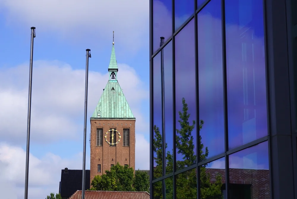 Kirchturm der Pfarrkirche St. Cyriakus neben der blau-violett spiegelnden Glasfassade des Rathauses in Weeze