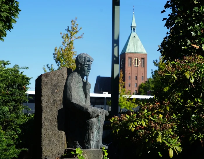 Skulptur im Grünen mit dem Kirchturm von St. Cyriakus im Hintergrund in Weeze