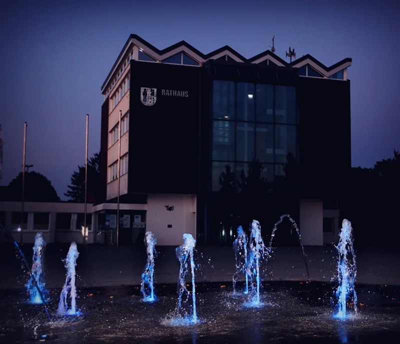 Rathaus in Weeze am Abend mit blau beleuchteten Wasserfontänen im Vordergrund