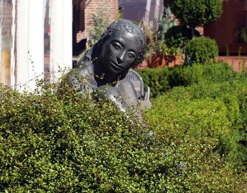 Im September zunehmend von Sträuchern überwachsene Skulptur einer Frau