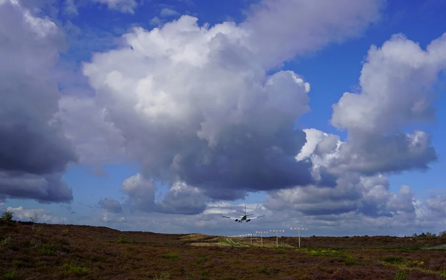 Landendes Flugzeug über der Heidelandschaft am Airport Weeze unter beeindruckenden großen Wolken.