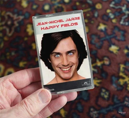 Fan-Art-Motiv von teddynash: Eine Hand hält eine fiktive Musikkassette mit dem Titel „Happy Fields“ von Jean-Michel Jarre. Das Cover zeigt ein humorvoll verfremdetes Porträt des jungen Musikers mit auffallend blauen Augen.