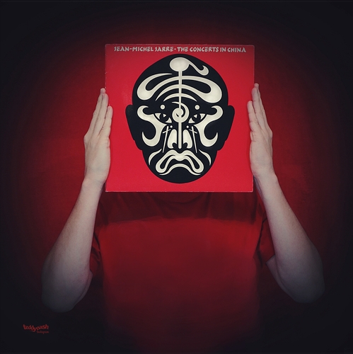 Fan-Art-Fotografie von teddynash: Eine Person hält die Schallplatte „The Concerts in China“ vor das Gesicht, sodass das markante Albumcover die Person vollständig ersetzt. Der rote Hintergrund greift die Farbwelt des Albums auf.