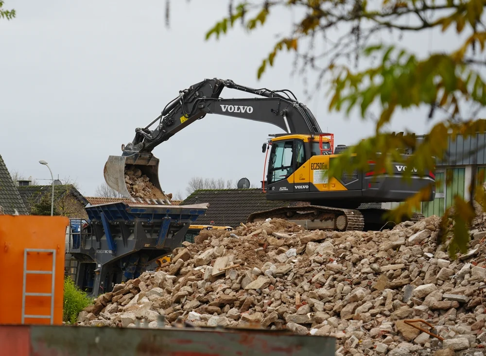 Ein Volvo-Bagger lädt den Abbruchschutt der alten Schule in eine Brechanlage zum Recycling.