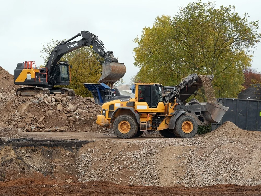 Große Volvo-Baumaschinen recyceln den Abbruchschutt der alten Schule – Beton und Steine werden direkt vor Ort weiterverarbeitet.