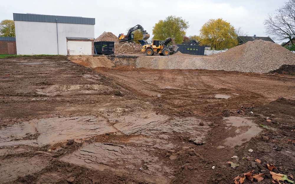 Im Vordergrund entsteht der neue Schulhof, während im Hintergrund große Baumaschinen den Abbruchschutt der alten Schule recyceln.
