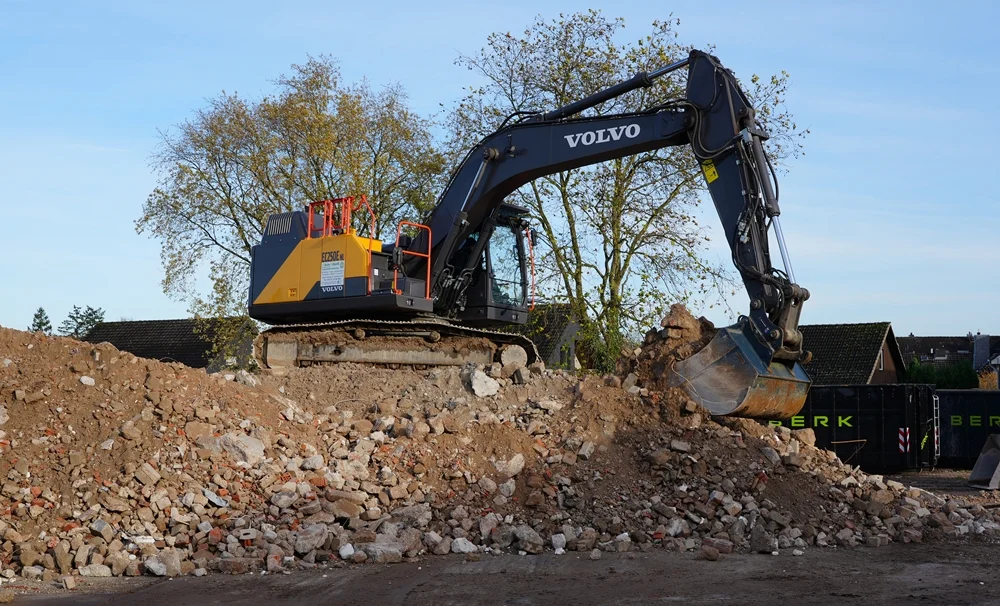 Ein mächtiger Volvo-Bagger arbeitet auf einem riesigen Schuttberg aus Beton- und Steinresten des Schulabbruchs in Weeze.