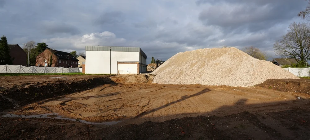 Dramatische Wolkenstimmung über dem leergeräumten Schulgelände mit großem Schuttberg und der alten Sporthalle im Hintergrund.