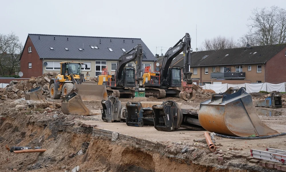 Auf dem früheren Schulhof der Johannes-Hauptschule stehen mehrere Volvo-Bagger und schwere Maschinen zwischen Schutt und freigelegten Fundamenten.