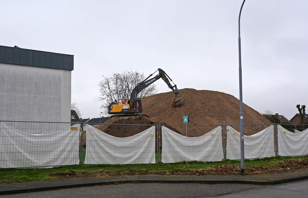 Ein Volvo-Bagger arbeitet auf einem riesigen Berg aus zerkleinertem Schutt hinter dem Bauzaun der Baustelle in Weeze.