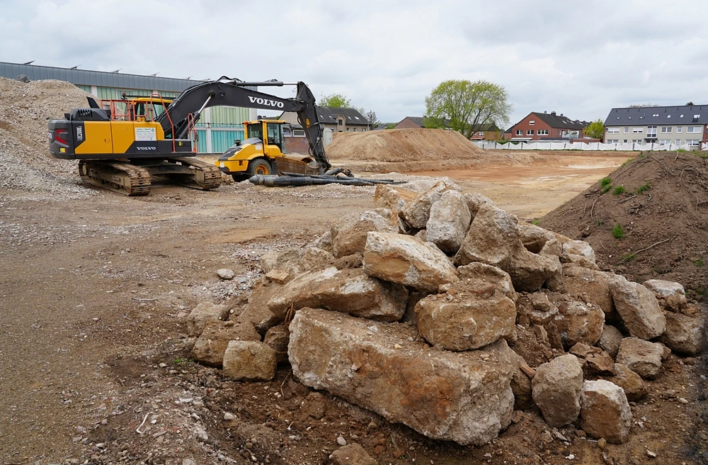 Große freigelegte Beton- und Steinbrocken liegen im Vordergrund der ehemaligen Schulbaustelle in Weeze, während im Hintergrund noch Maschinen arbeiten.