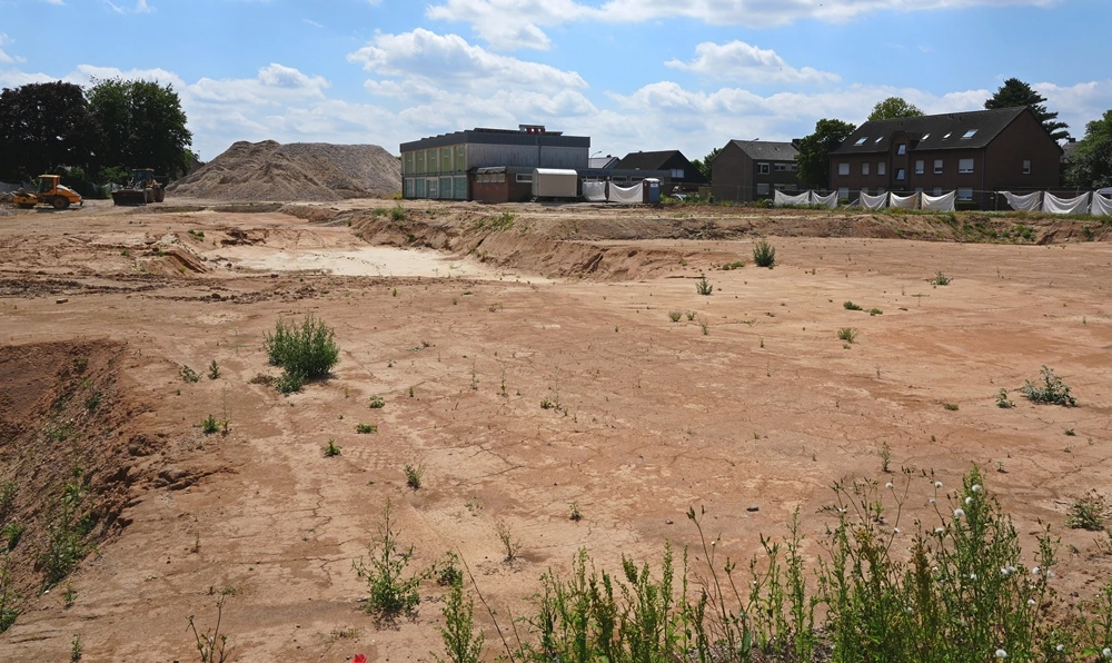 Freie Baufläche der ehemaligen Johannes-Hauptschule in Weeze nach dem Abriss. Im Hintergrund liegen große Schotterberge und die alte Sporthalle.