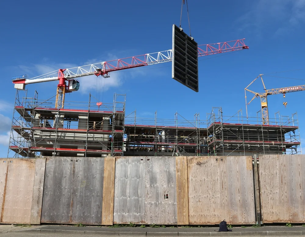 Ein Kran hebt eine große Wandschalung über die Baustelle der neuen PC-Grundschule in Weeze