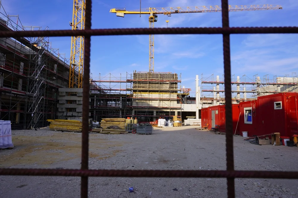 Blick durch den Bauzaun auf die Baustelle der neuen Petrus-Canisius-Grundschule in Weeze mit Baukränen, Rohbau und Baustellencontainern.