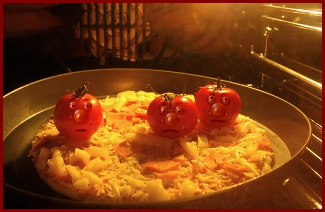 Drei Tomaten mit Gesichtern sitzen auf einer Pizza im Backofen. Die humorvolle Szene zeigt ihre besorgten Blicke kurz vor dem Backen.