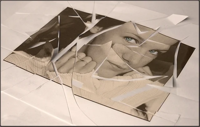 Ein Porträtfoto einer Frau liegt in zahlreiche Fragmente zerbrochen aufgeteilt auf einer hellen Oberfläche. Die Komposition spielt mit Spiegelungen, Erinnerung und Zerbrechlichkeit.